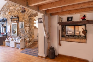 A rustic interior with a stone wall, wooden beams, a fireplace, and a display of books and pottery. - Le Loft de L'Île - A 250m de la Plage (L'Île-Rousse)