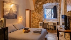Ein Schlafzimmer mit Bett, Schreibtisch, Stuhl, Fernseher und einer Steinwand.