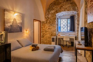 A bedroom with a bed, a desk, a chair, a TV, and a stone wall. - Le Loft de L'Île - A 250m de la Plage (L'Île-Rousse)