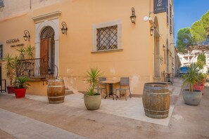 A building with a sign reading 'OSTERIA' and a wooden door. There are potted plants, a table with chairs, and a window with a metal grille. - Le Loft de L'Île - A 250m de la Plage (L'Île-Rousse)