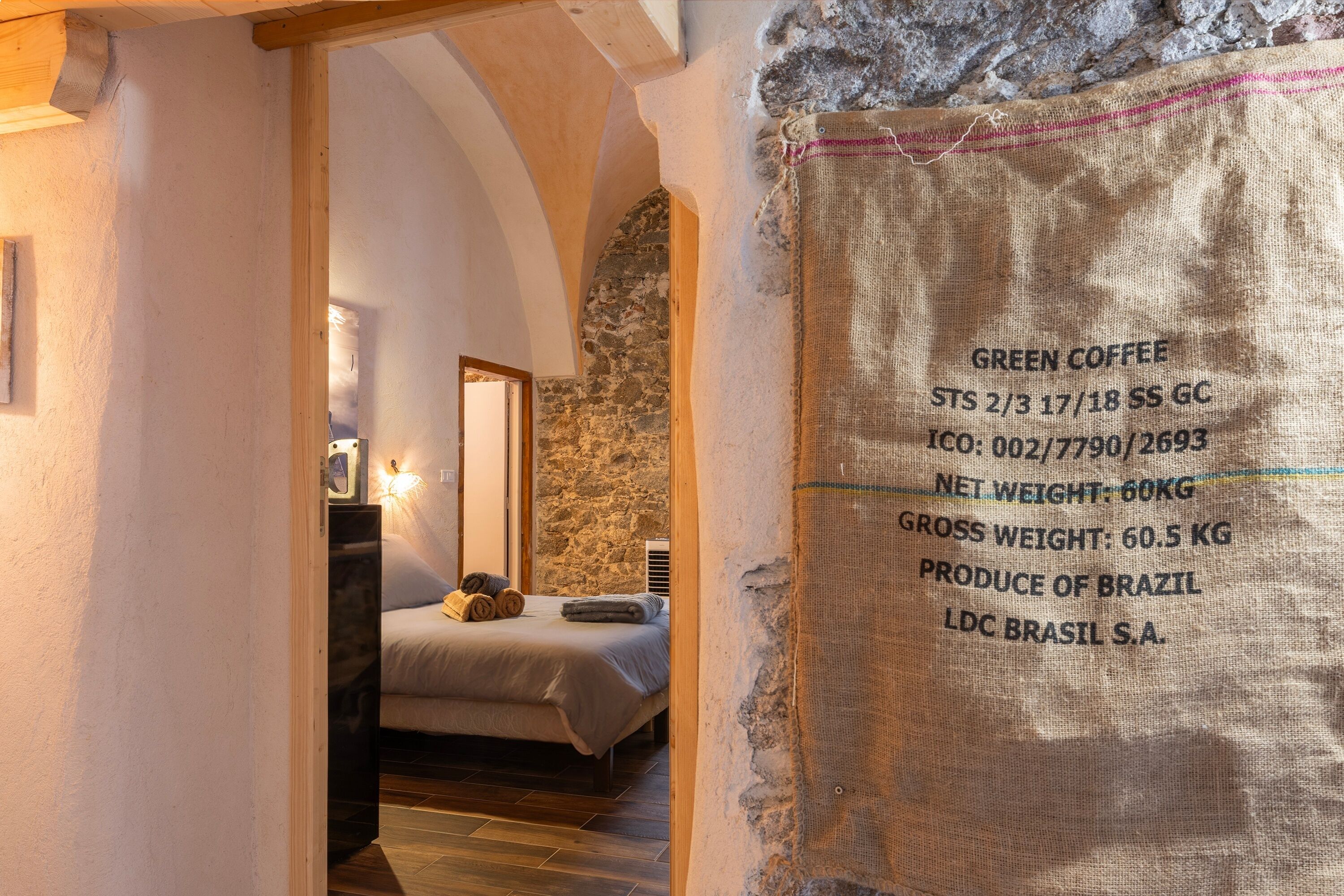 Une pièce avec un lit, une table de chevet et un mur en pierre. On y voit une pancarte avec du texte.