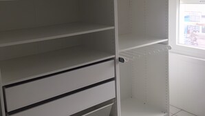 Ein Zimmer mit weißem Kleiderschrank, Heizkörper und einem Fenster mit Jalousien.