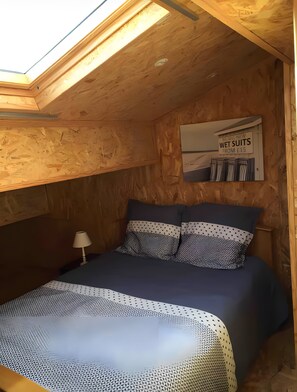 Un dormitorio con tragaluz, una cama con ropa de cama estampada y un cartel publicando trajes de neopreno.