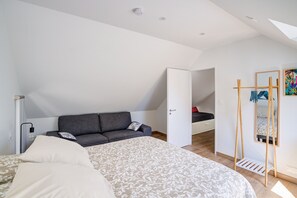 Un dormitorio con una cama, un sofá gris, una escalera de madera y una puerta que da a otra habitación.
