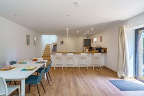 Una cocina moderna con una isla central, suelo de madera y un comedor con sillas y una mesa dispuesta para una comida.