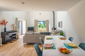 Ein modernes Wohnzimmer mit Klavier, Fernseher und Essbereich mit Tisch für zwei Personen.