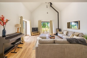 A spacious living room with a piano, sofa, TV, and a large window offering a view of greenery. - L'Escapade Odet - Gîte avec terrasse et jardin (Gouesnach)