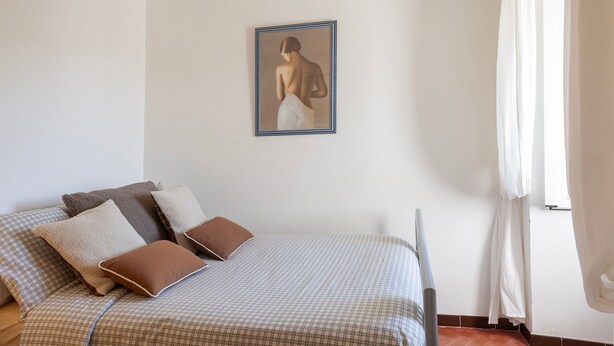 Un dormitorio con cama, almohadas, un cuadro enmarcado en la pared y una ventana con cortinas.