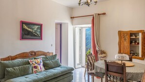 Una habitación con un sofá verde, un armario de madera, una mesa de comedor con mantel a cuadros y una araña.