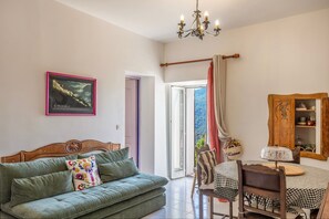 A room with a green sofa, a wooden cabinet, a dining table with a checkered tablecloth, and a chandelier. - Le Refuge d'U Casone - Balcon avec jolie vue (Crocicchia)