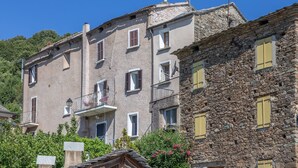 Un edificio de varios pisos con fachada de piedra y enlucido, balcones y ventanas con contraventanas.