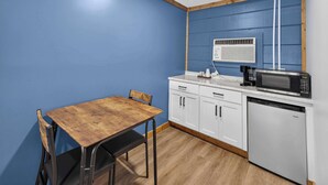 Una cocina compacta con una mesa de madera, armarios blancos, un microondas y un refrigerador pequeño.