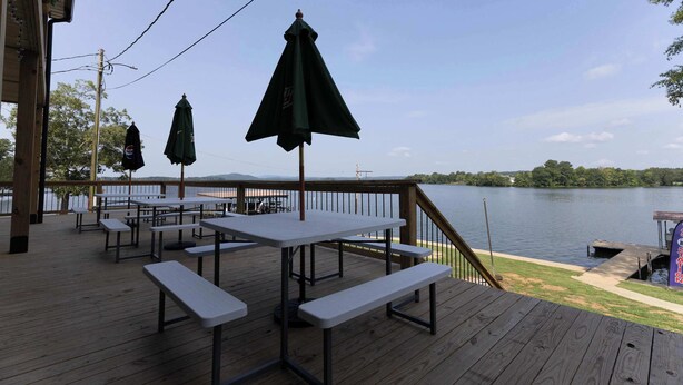 Terraza de madera con mesas de picnic y sombrillas con vistas a un lago.