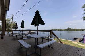 Terraza de madera con mesas de picnic y sombrillas con vistas a un lago.