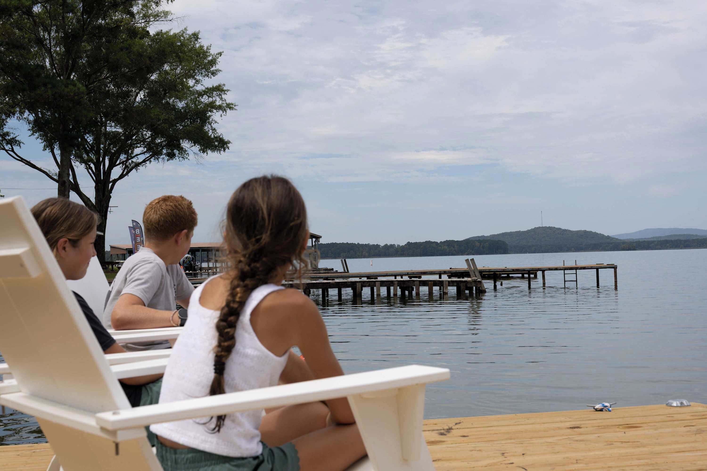 A lakeside setting with a wooden dock extending into the water, surrounded by trees and a distant hill.
