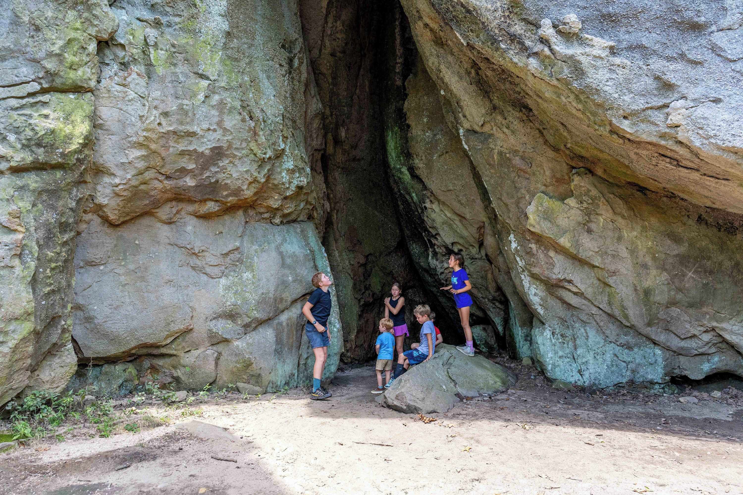 Un grupo de personas frente a una gran formación rocosa con una abertura parecida a una cueva.