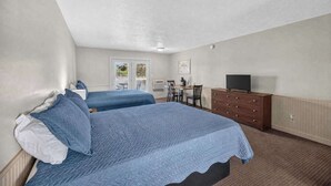 Quarto de hotel com duas camas, uma cômoda, televisão e janela com vista.