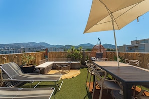 Eine Dachterrasse mit Gartenmöbeln, einem Tisch und einem großen Sonnenschirm.
