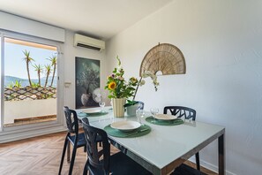 Ein Essbereich mit einem Tisch für zwei Personen, Stühlen, einer Blumenvase und einem Wandventilator.