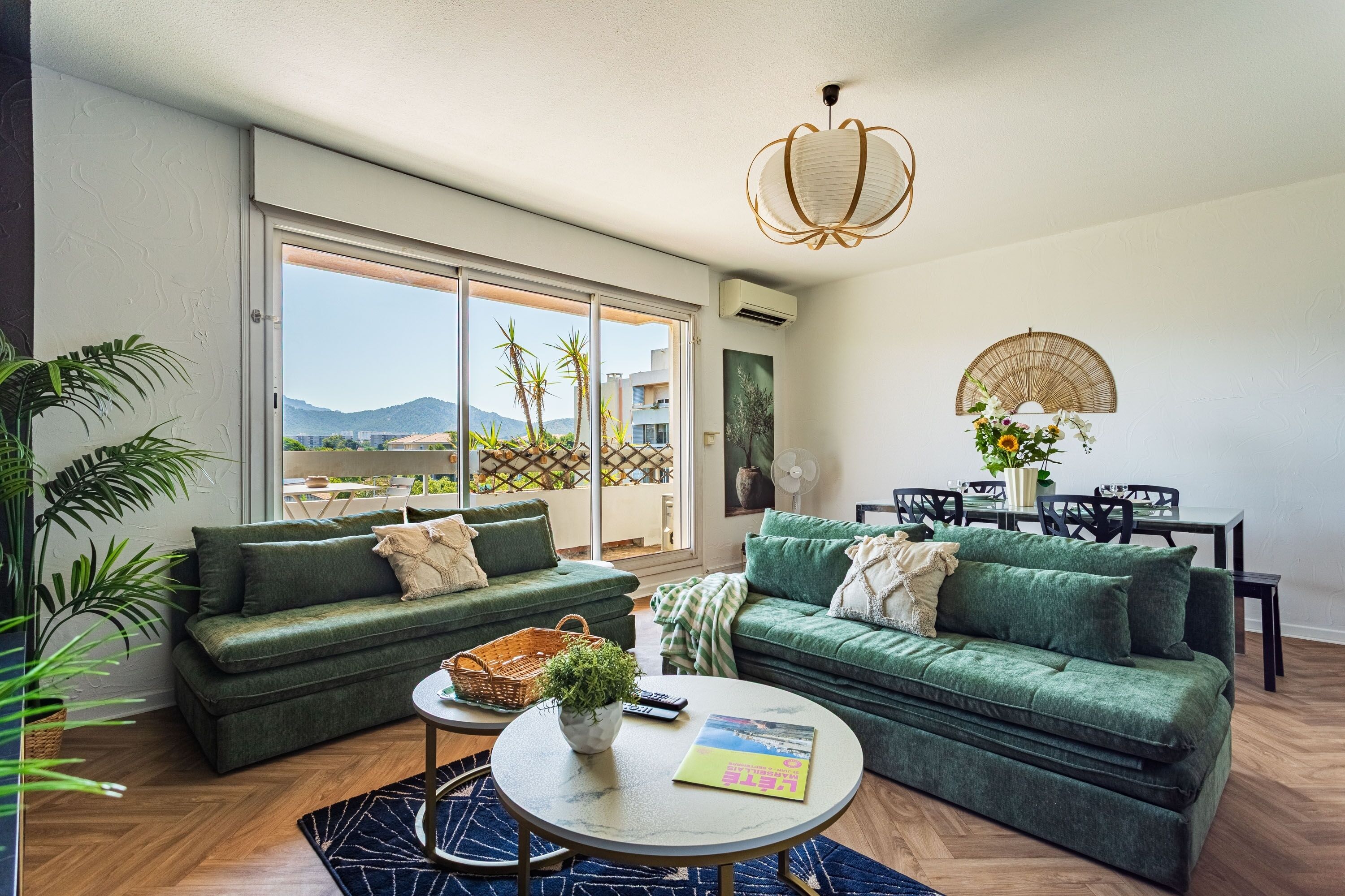A modern living room with two green sofas, a coffee table, and a dining area with a table and chairs.