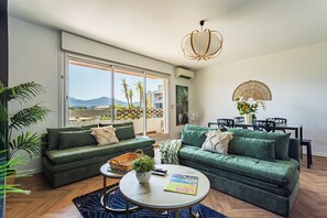 Ein modernes Wohnzimmer mit zwei grünen Sofas, einem Couchtisch und einem Essbereich mit Tisch und Stühlen.