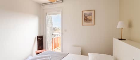 A hotel room with a bed, a window with a view, a framed picture on the wall, and a lamp.