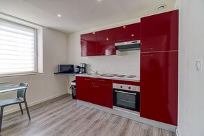 Eine kleine Küche mit roten Schränken, einer Mikrowelle, einer Kaffeemaschine und einem eingebauten Backofen.