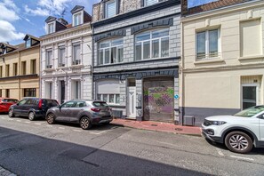 A street view with parked cars, a building with a garage door, and a clear sky. - Le Central - Appt pour 2 en plein cœur de Calais (Calais)