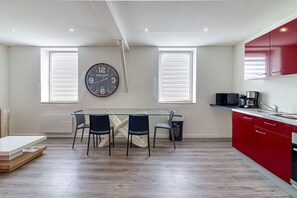 A modern kitchen with a glass dining table, two chairs, a red cabinet, and a wall clock. - Le Central - Appt pour 2 en plein cœur de Calais (Calais)