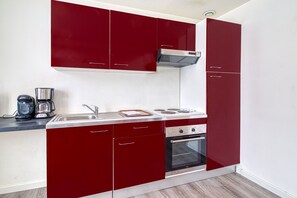 A compact kitchen with red cabinets, a sink, a stove, and a coffee maker. - Le Central - Appt pour 2 en plein cœur de Calais (Calais)