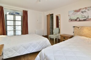 Un dormitorio con dos camas, una silla, una mesita de noche, un radiador y una ventana con cortinas.