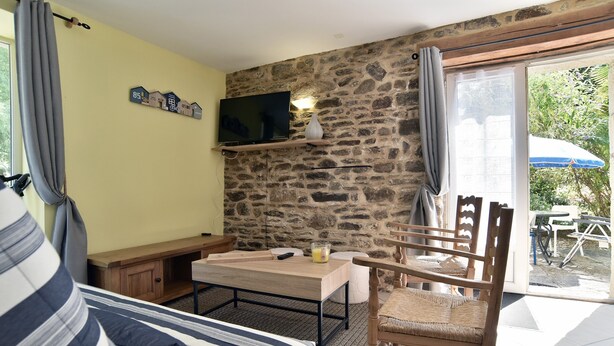 Ein gemütliches Wohnzimmer mit einer Steinsäule, einem Flachbildfernseher über einem Holztisch, einem Korbsessel und einem Sofa mit gestreiften Kissen.