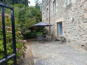 A stone building with a patio area featuring outdoor furniture and a table with an umbrella. - Degas - Appt pour 6 avec terrasse et parking (Dinan)