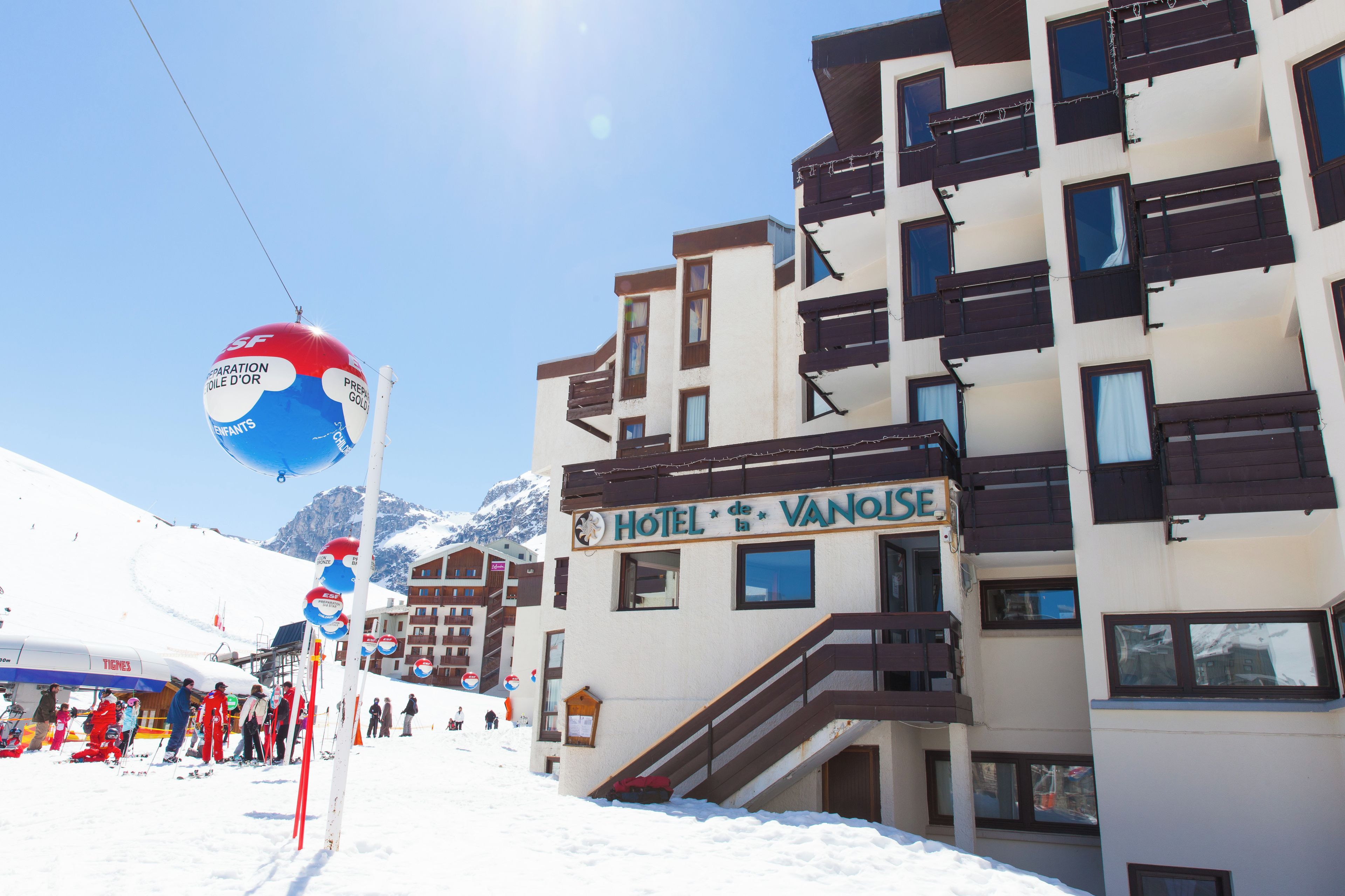 Een hotel met een bord waarop 'HOTEL DE LA VANOLSE' staat, en een skipiste op de achtergrond.