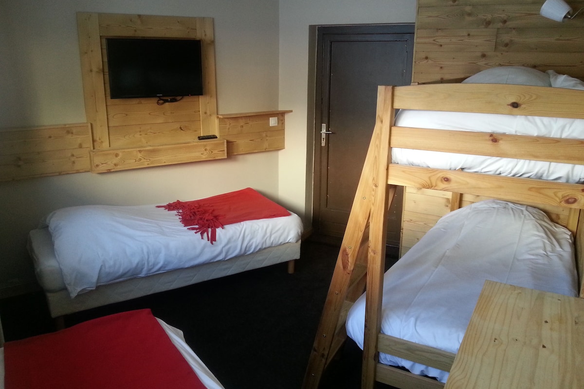 A room with a bunk bed, a single bed, a wooden headboard, a television mounted on the wall, and a door.