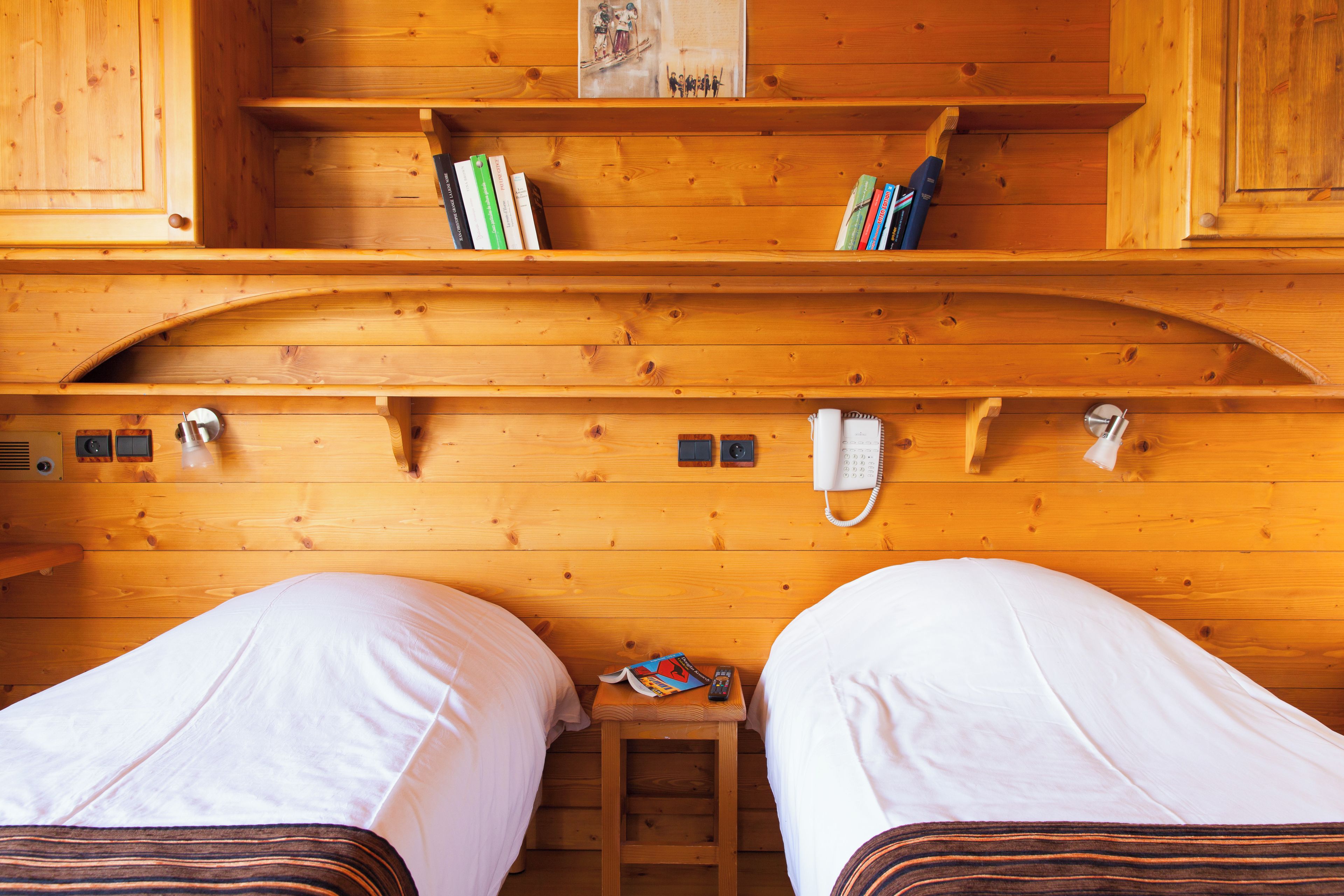 Ein Holzblockhaus-Interieur mit zwei Betten, einem Bücherregal, einem kleinen Tisch mit einer Fernbedienung und einem Telefon an der Wand.