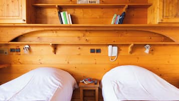 Ein Holzblockhaus-Interieur mit zwei Betten, einem Bücherregal, einem kleinen Tisch mit einer Fernbedienung und einem Telefon an der Wand.