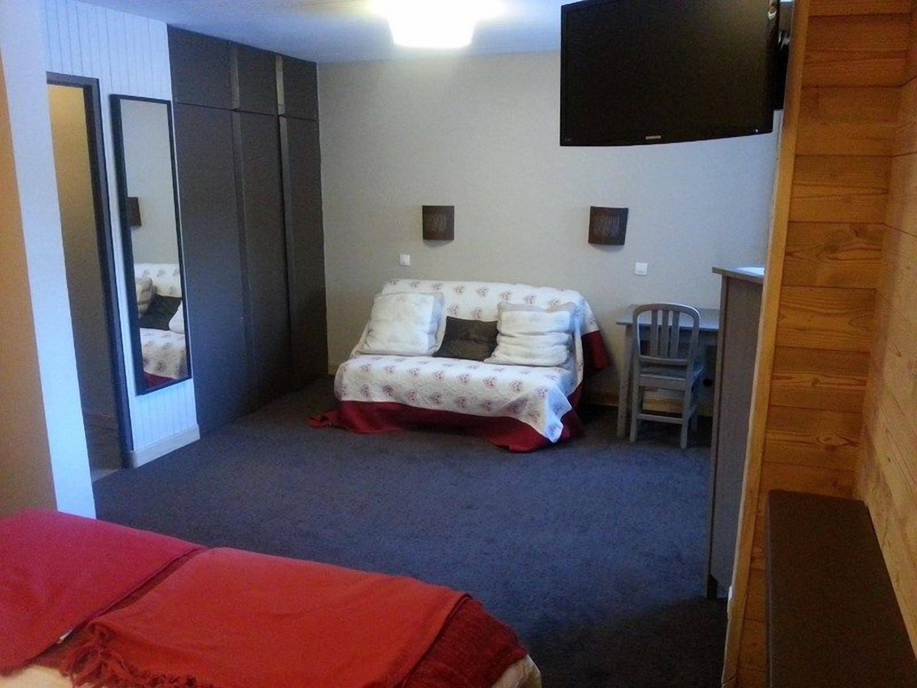 A bedroom with a bed, a mirror, a TV, and a desk.