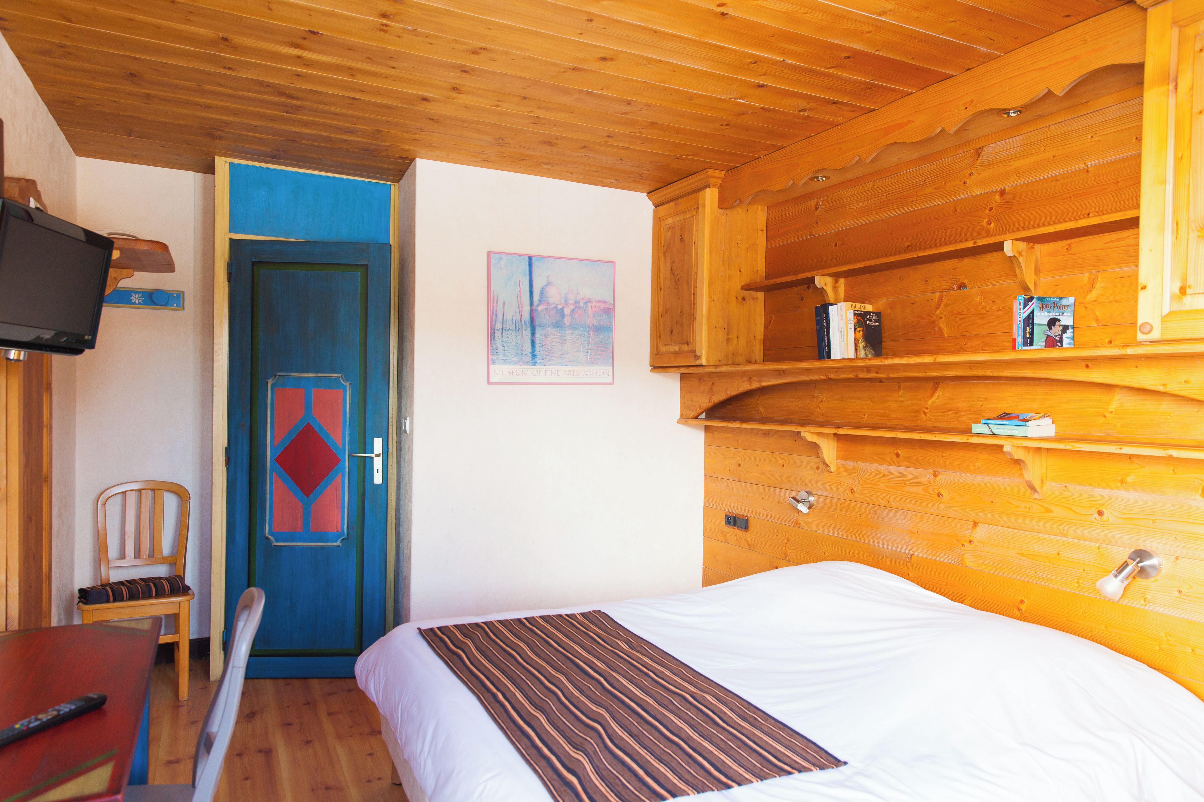 Ein Zimmer mit Holzboden, einem Bett, einem Sessel, einem Fernseher und einer Tür mit blauer Umrandung.