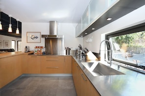 Eine moderne Küche mit Dunstabzugshaube aus Edelstahl, Holzschränken, einem großen Fenster und Blick ins Freie.