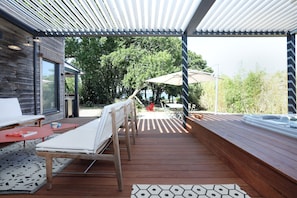 Eine überdachte Terrasse im Freien mit Whirlpool, Liegestühlen und einem Tisch.