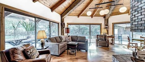 A spacious living area with a high ceiling, large windows, and a fireplace.