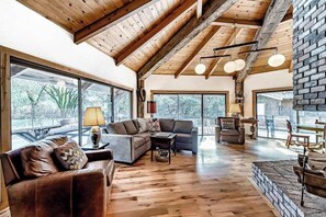 A spacious living area with a high ceiling, large windows, and a fireplace.