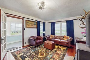 Ein Wohnzimmer mit einer braunen Ledersofa-Garnitur, einem gemusterten Teppich und einem großen Fenster mit blauen Vorhängen.