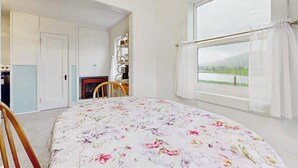 Ein Schlafzimmer mit einem Bett, einem Vorhangfenster, einem Sessel und einer Tür zu einem weiteren Raum.