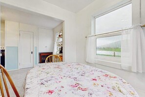 Ein Schlafzimmer mit einem Bett, einem Vorhangfenster, einem Sessel und einer Tür zu einem weiteren Raum.