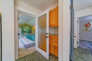 A hallway leading to a swimming pool with a door to a room with wooden cabinets.