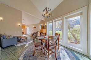 A spacious living area with a dining table, chairs, and a sofa. There are large windows providing natural light and a view of the outdoors. - The Pool House - Private Pool & Relaxing Outdoor Retreat (Ferndale)