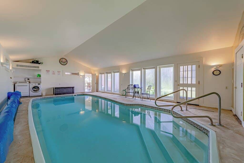 A swimming pool with a sunlit interior, a seating area with chairs, and a visible laundry area.