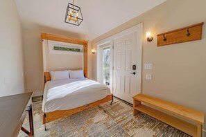 A bedroom with a bed, a bench, a door, and a wall-mounted shelf.